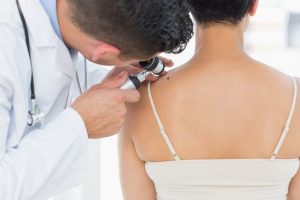 Male dermatologist examining mole on back of woman in clinic
