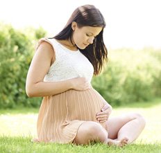 Pregnant woman sits on grass holding stomach