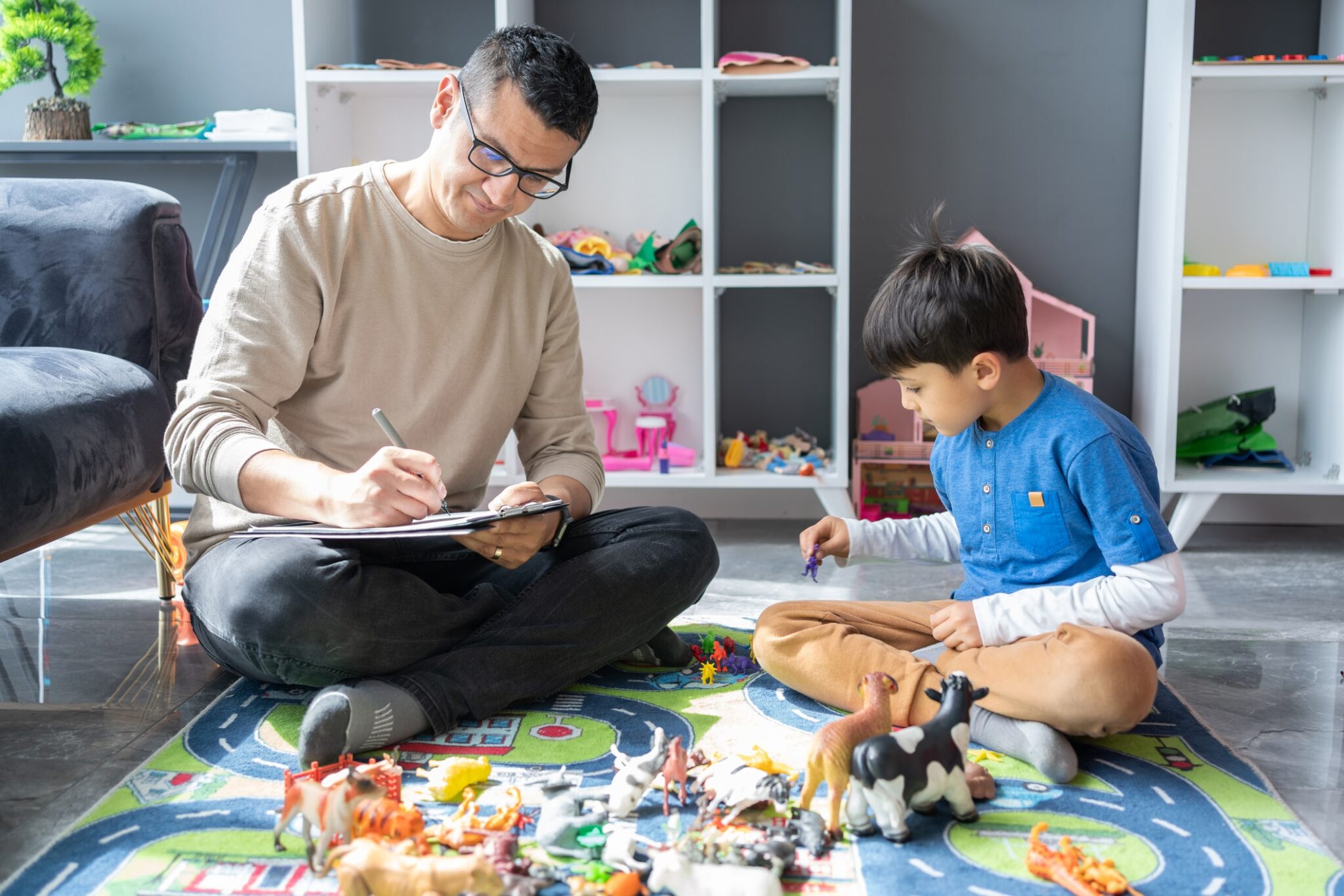 man writes observations about child while he plays with toys