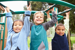 three young boys hanging on jungle gym bars on the playground after being vaccinated for measles