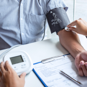 A man sitting at a desk has his blood pressure taken from a health care professional providing chronic disease management