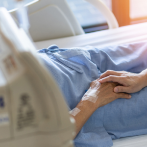 A caregiver or loved one holds the hand of a patient in a hospital bed receiving palliative care