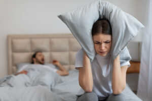 Woman covering ears with pillow due to man snoring as a result of obstructive sleep apnea